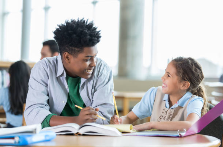 High school student tutoring a younger student at a library table